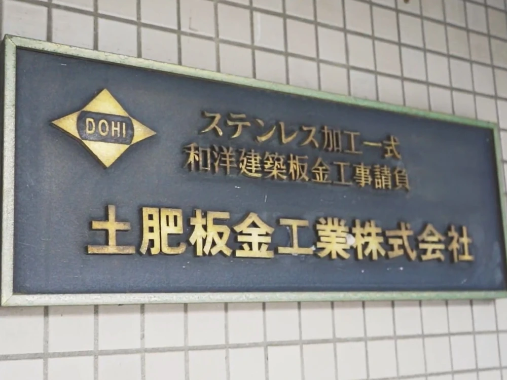 土肥板金工業株式会社の社名看板。ステンレス加工一式、和洋建築板金工事請負の文字が刻まれた金属製のプレート